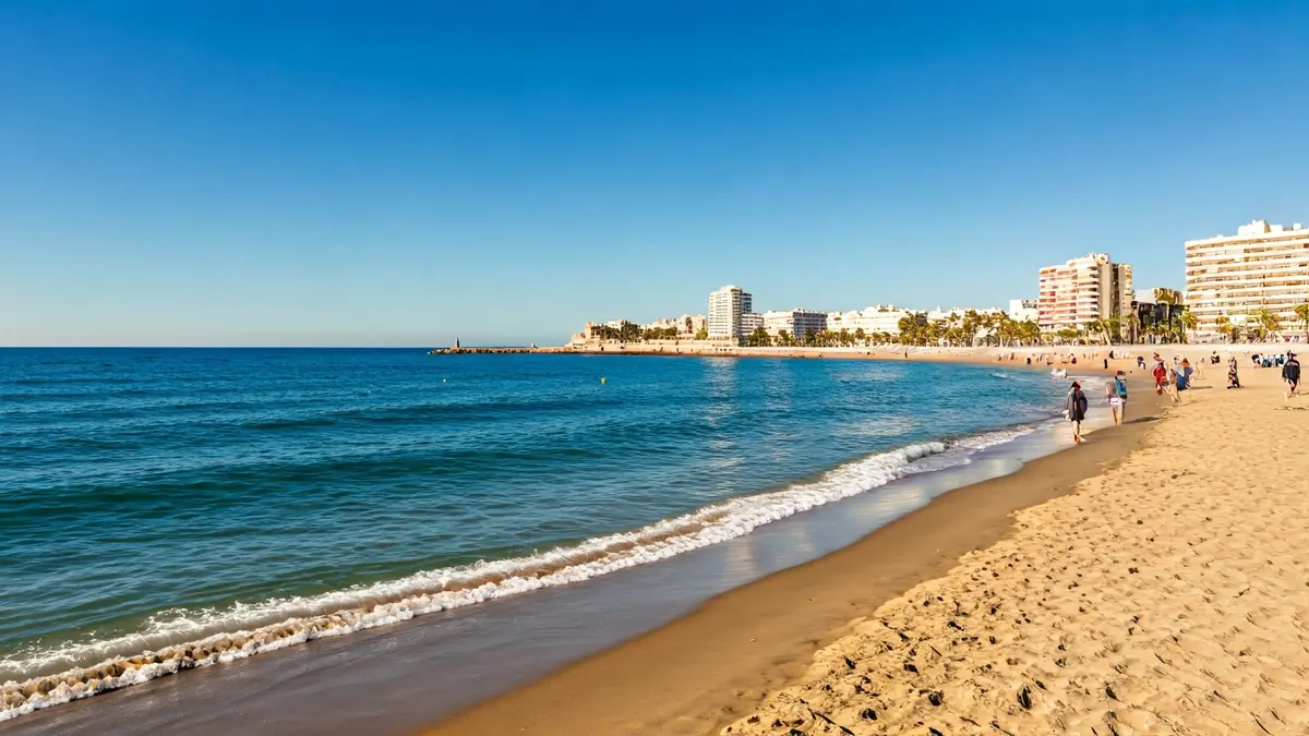 Generic image of a sunny beach in the Comunitat Valenciana with a few people walking along the seashore.