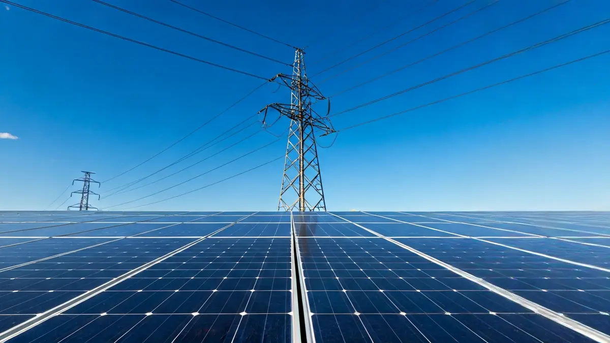 Generic image of an electricity pylon with solar panels in the background, symbolizing energy transition.
