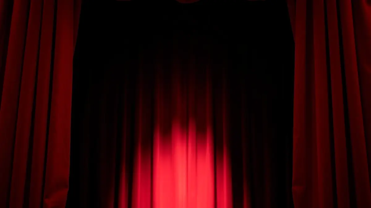 Imatge genèrica d'un escenari de teatre amb cortines de vellut roig, suggerint una representació.