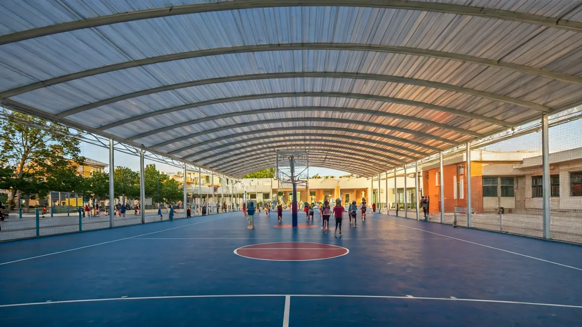 Imagen de una cancha de baloncesto cubierta junto a una escuela.