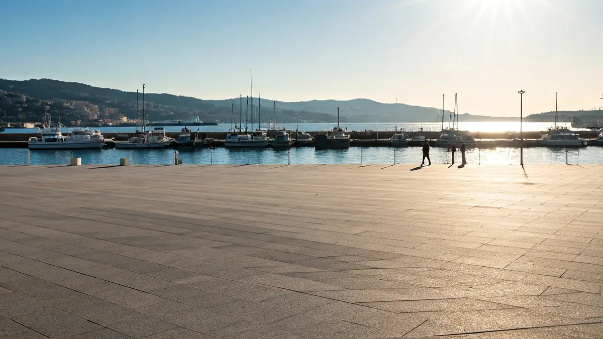 Imatge d'una plaça pública moderna i accessible al costat del mar en un entorn portuari.