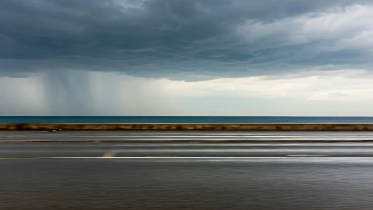 Generic image of a Mediterranean coastal landscape under a grey, stormy sky, with heavy rain and a muddy puddle.