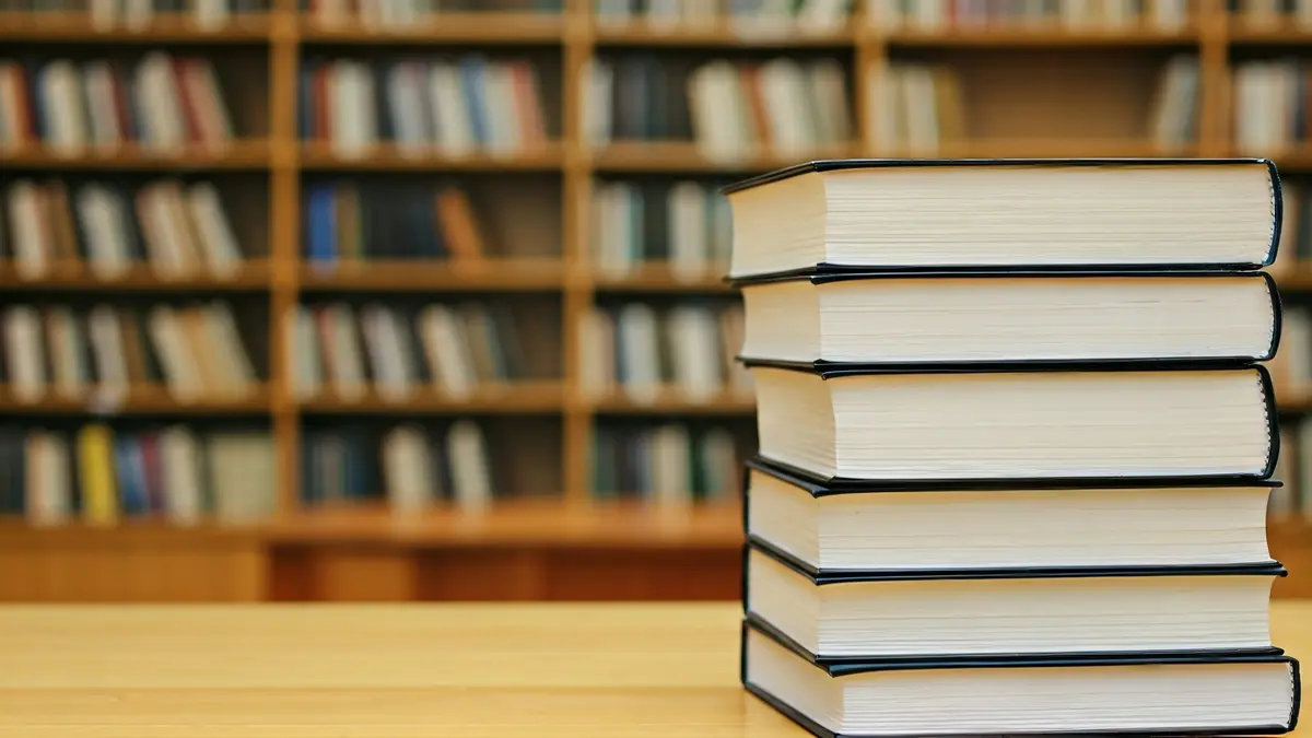 Generic image of a stack of books in a library, with warm light.