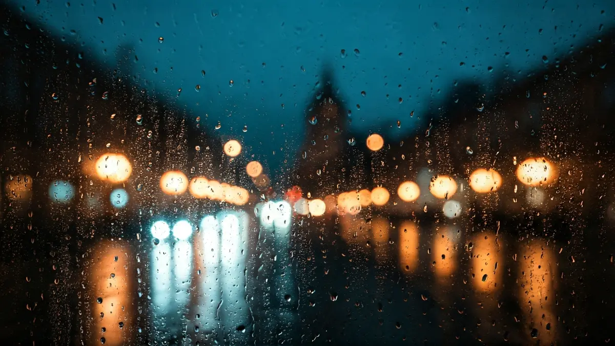 Imagen genérica de lluvia cayendo sobre un cristal con luces de ciudad desenfocadas al fondo.