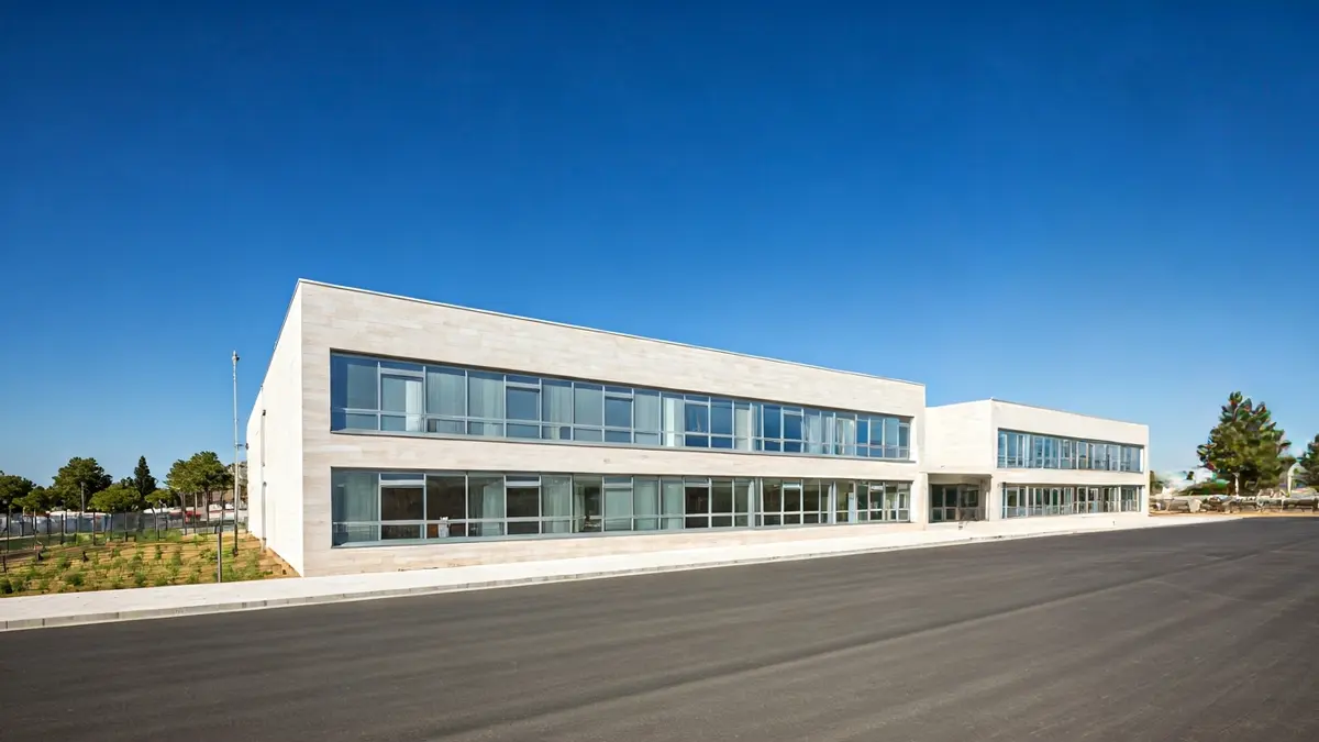 Imatge d'un edifici escolar modern amb grans finestrals i un disseny net, sota un cel blau clar en un paisatge mediterrani.