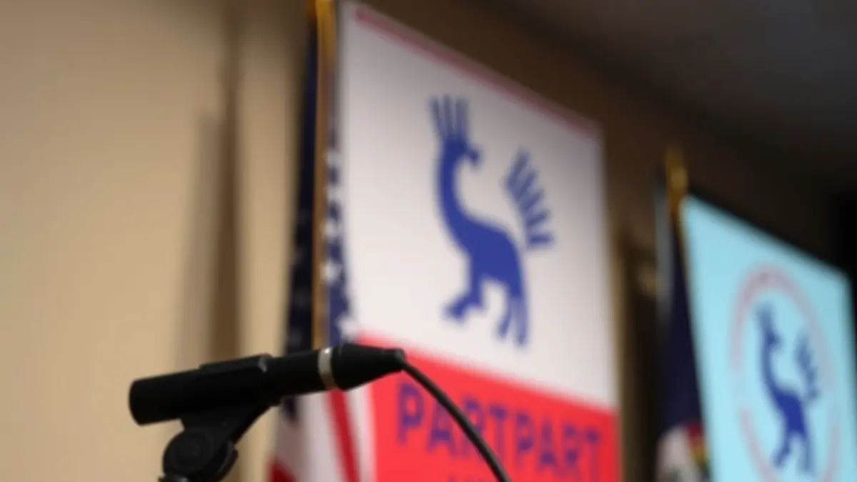 Generic image of a podium with microphones in front of a blurred political party logo, in a formal setting.