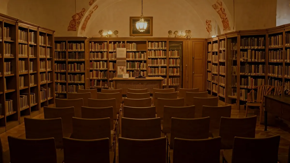 Imatge genèrica d'un interior de biblioteca amb prestatgeries de fusta i un faristol amb micròfon.