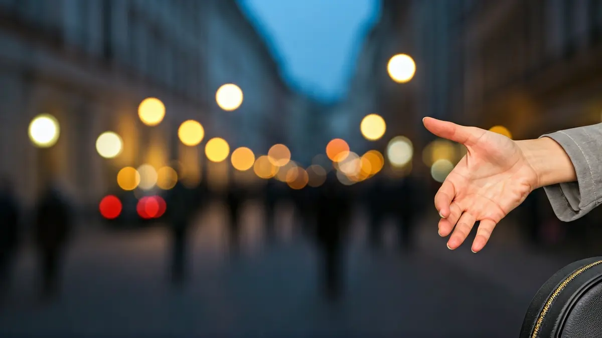 Imagen de una mano de mujer sosteniendo un bolso en una calle de ciudad al atardecer.