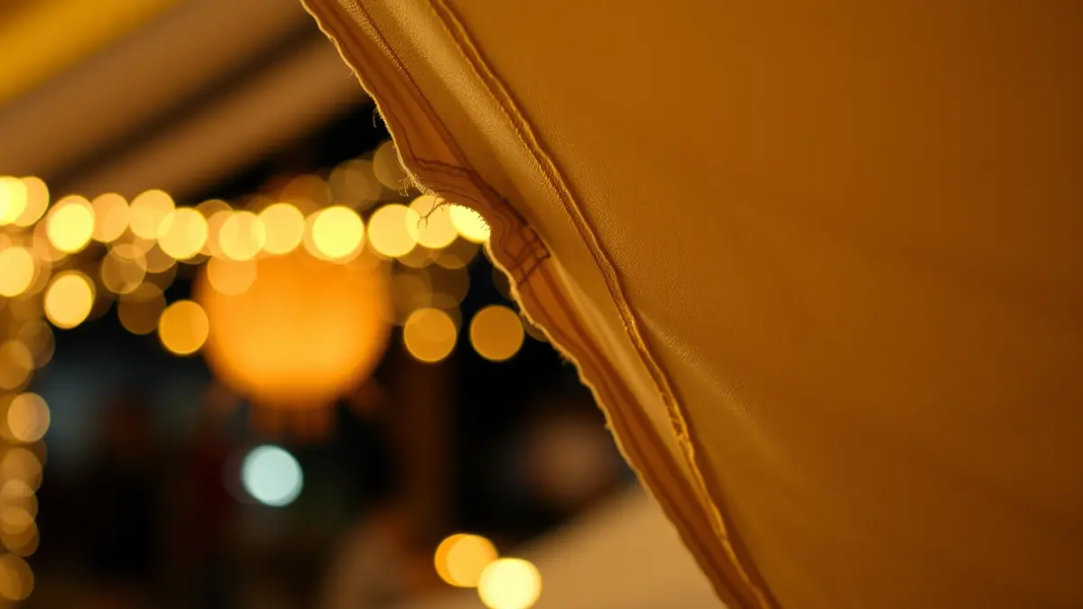 Imatge d'una lona de carpa fallera trencada, amb llums festives desenfocades al fons.