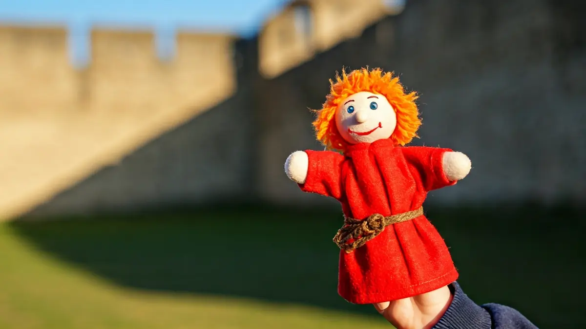 Image of a finger puppet on a child's hand with an ancient castle in the background.