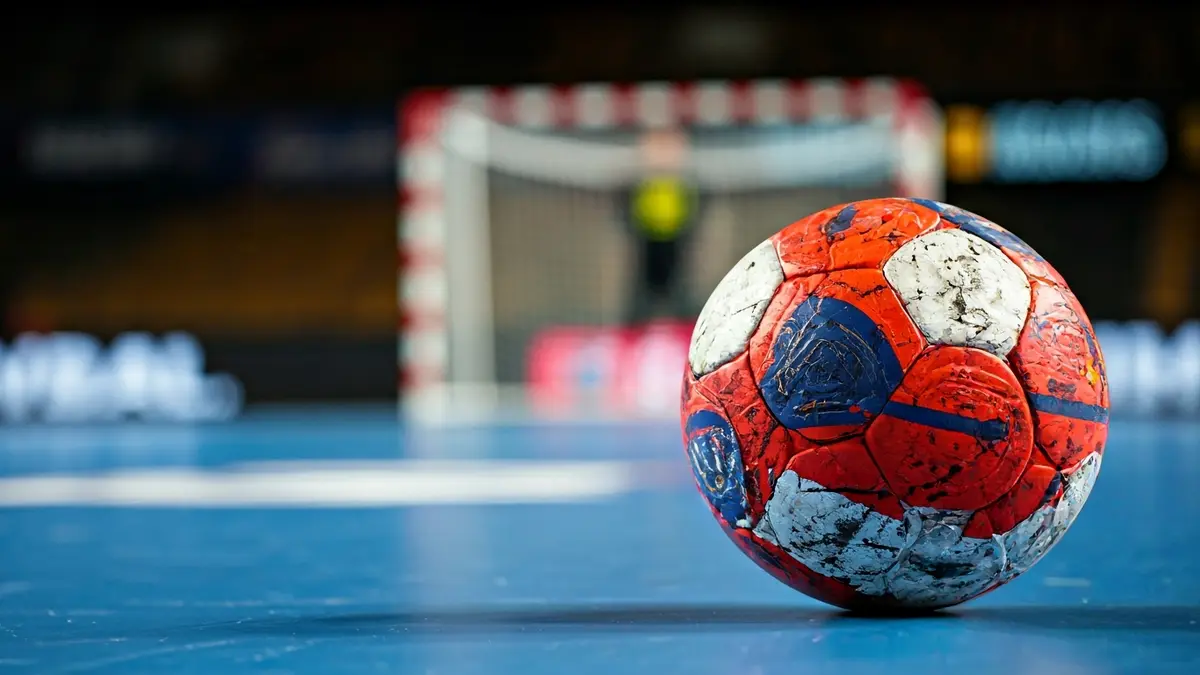 Imagen genérica de un balón de balonmano sobre la cancha, con la portería desenfocada al fondo.