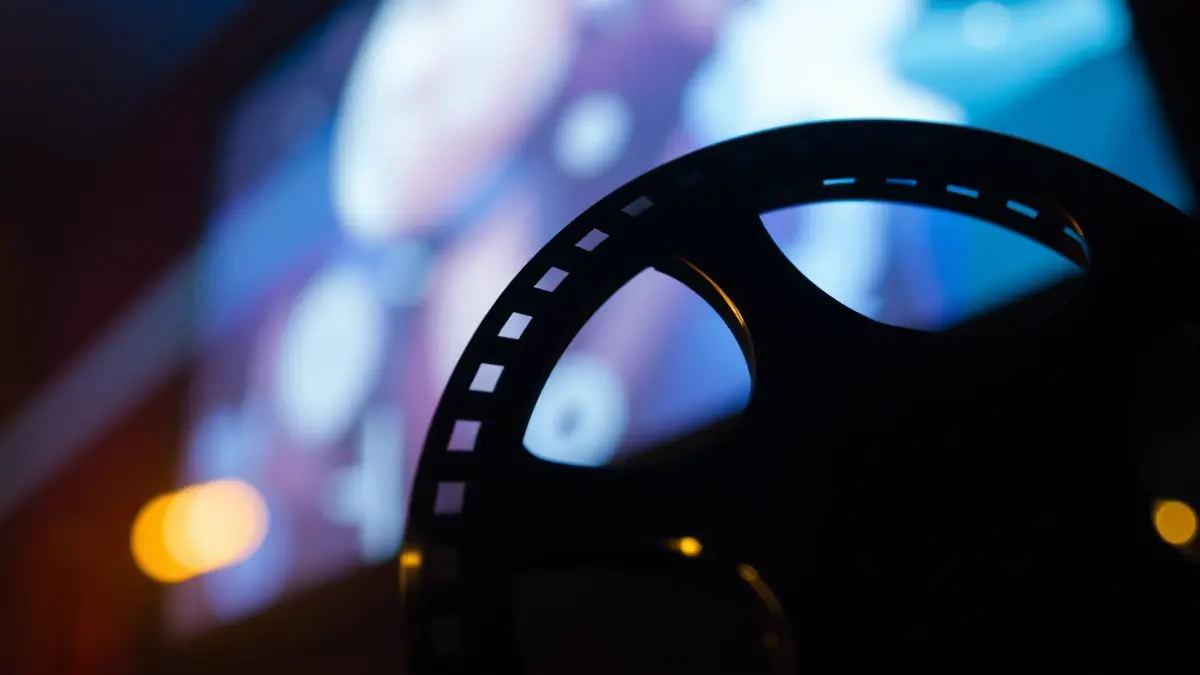 Imagen genérica de un carrete de película con luces borrosas de una pantalla de cine al fondo.