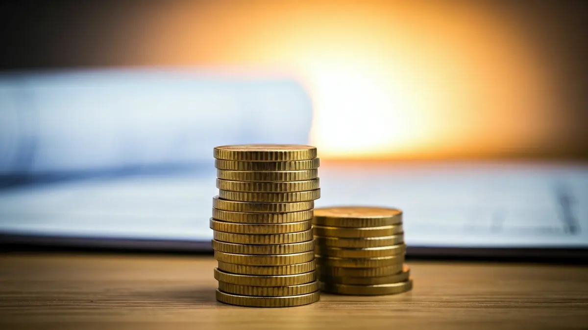 Imatge genèrica de monedes d'euro sobre una taula, amb plànols arquitectònics desenfocats al fons.