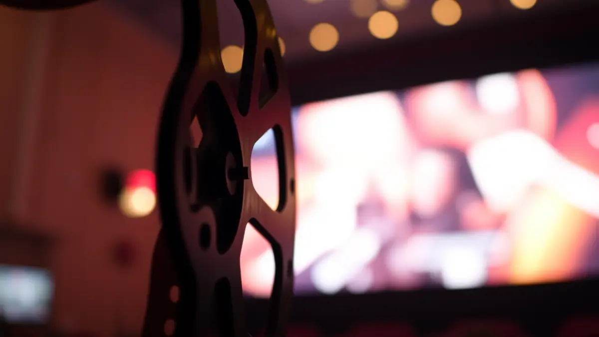 Generic image of a film reel with blurred lights of a cinema screen in the background.