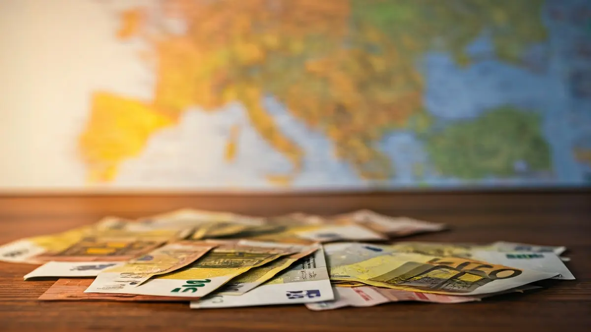 Generic image of various international currencies on a wooden table, with a blurred map of the Comunitat Valenciana in the background.
