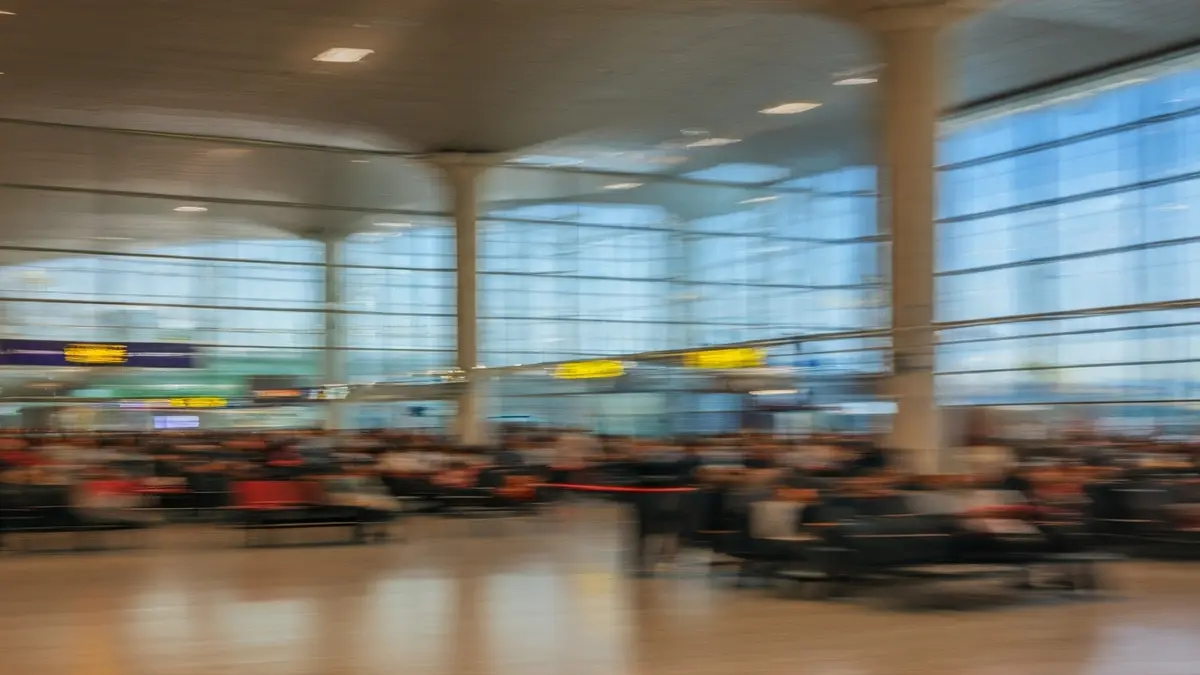 Imagen genérica del interior de un aeropuerto con pasajeros borrosos y grandes ventanales.