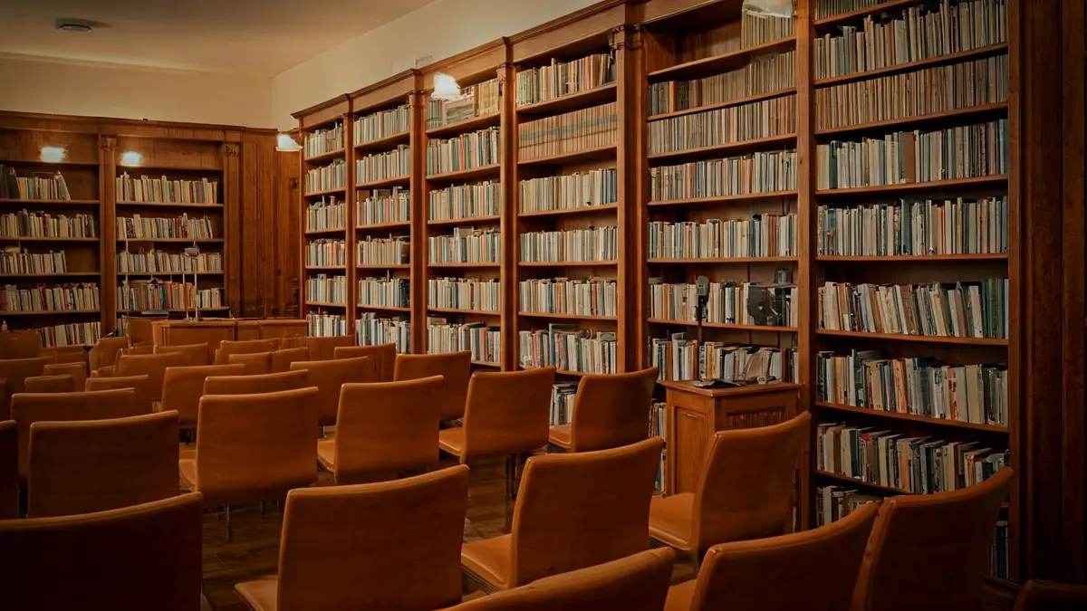 Imatge genèrica d'una biblioteca amb prestatgeries de fusta i un podi amb micròfon, amb una il·luminació càlida.