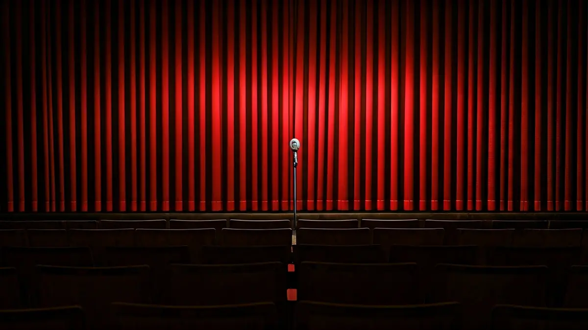 Imatge genèrica d'un escenari de teatre amb un micròfon i cortines de vellut roig.
