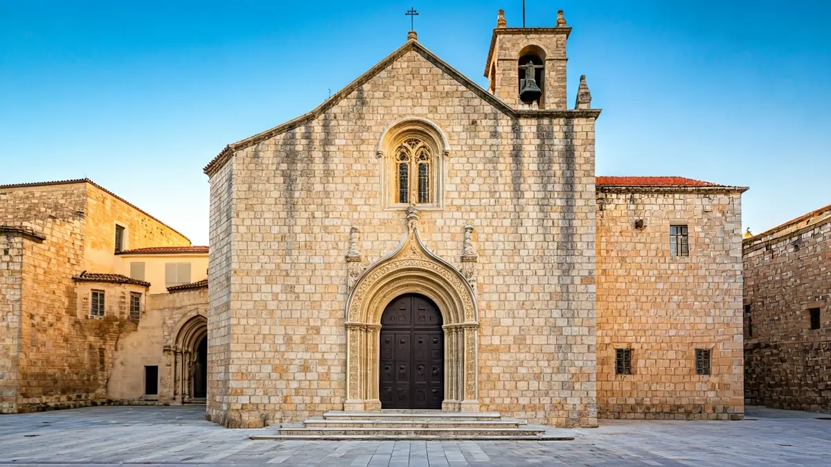 Fachada de piedra de un monasterio mediterráneo con detalles arquitectónicos, iluminada por el sol de la tarde.