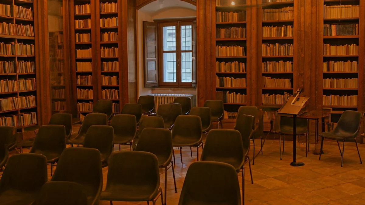 Imatge genèrica d'un interior de biblioteca amb prestatgeries de fusta i un faristol amb micròfon, il·luminació càlida.