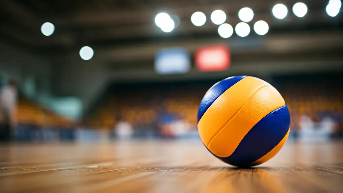 Imatge genèrica d'una pilota de voleibol en una pista de fusta, amb un fons desenfocat d'un pavelló esportiu.