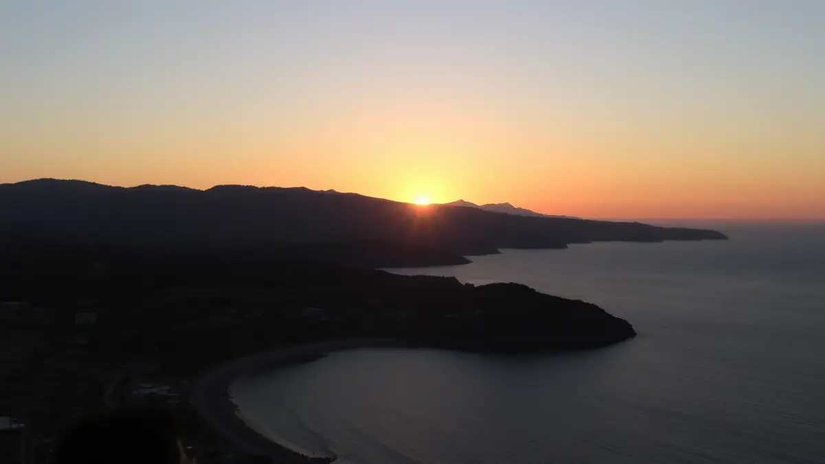 Imagen de un eclipse solar parcial en un paisaje costero mediterráneo al atardecer, con el sol bajo en el horizonte.