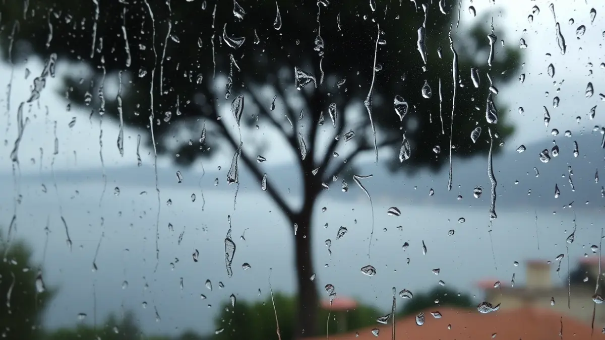 Generic image of rain falling on a window pane, with a blurred Mediterranean landscape in the background.