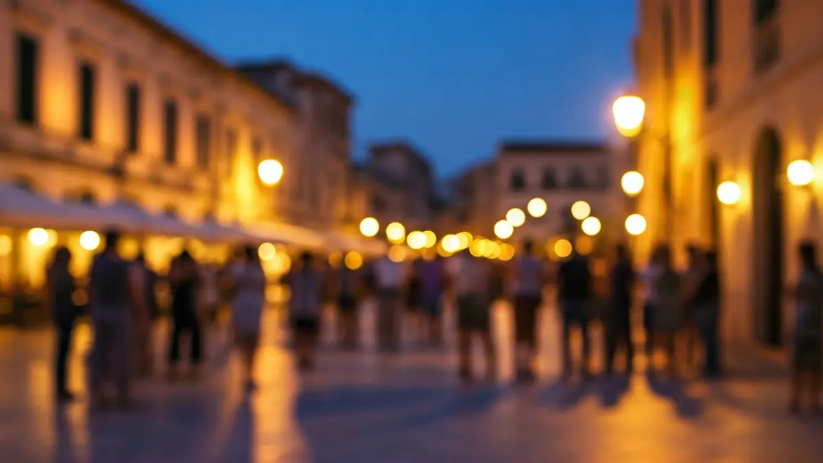 Imagen de una ciudad mediterránea con actividades artísticas nocturnas, luces y gente disfrutando del evento.