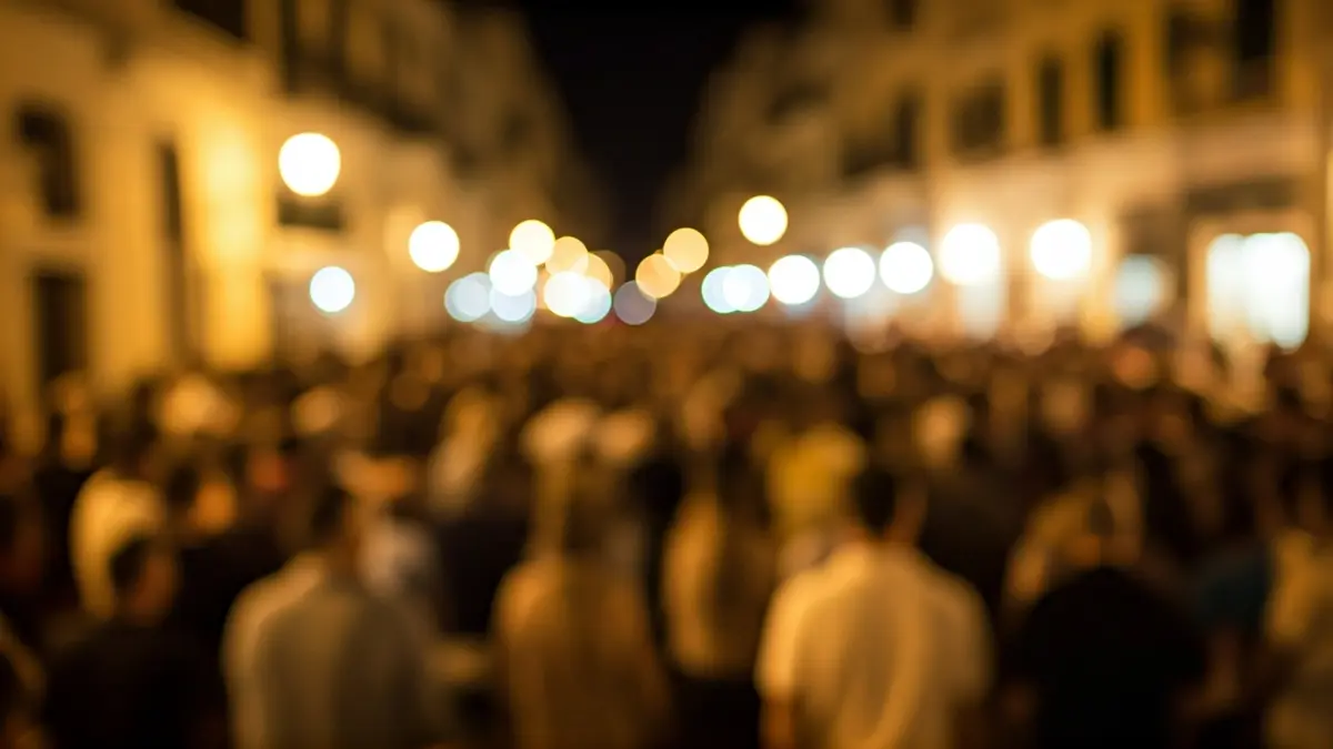 Imagen genérica de una multitud borrosa en una calle de ciudad mediterránea de noche, con luces cálidas.