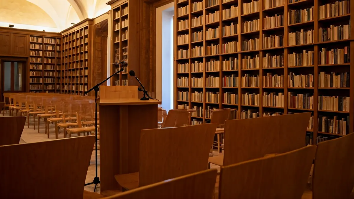 Imagen genérica de una sala de presentaciones o biblioteca con un atril y sillas vacías, iluminación cálida.
