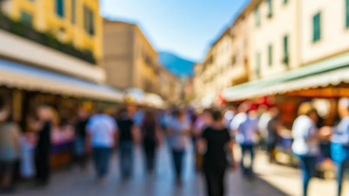 Imatge d'una fira popular en un carrer ple de gent en una ciutat mediterrània, amb edificis tradicionals i un cel clar.