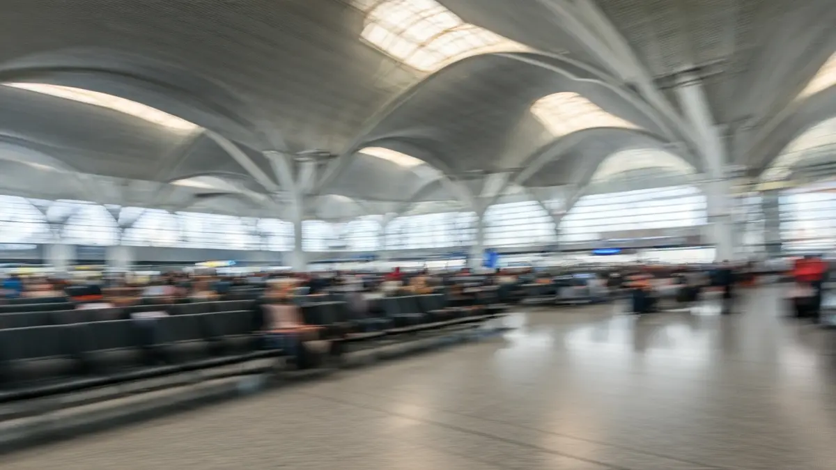 Imagen genérica del interior de una terminal de aeropuerto con pasajeros difuminados y luz natural.