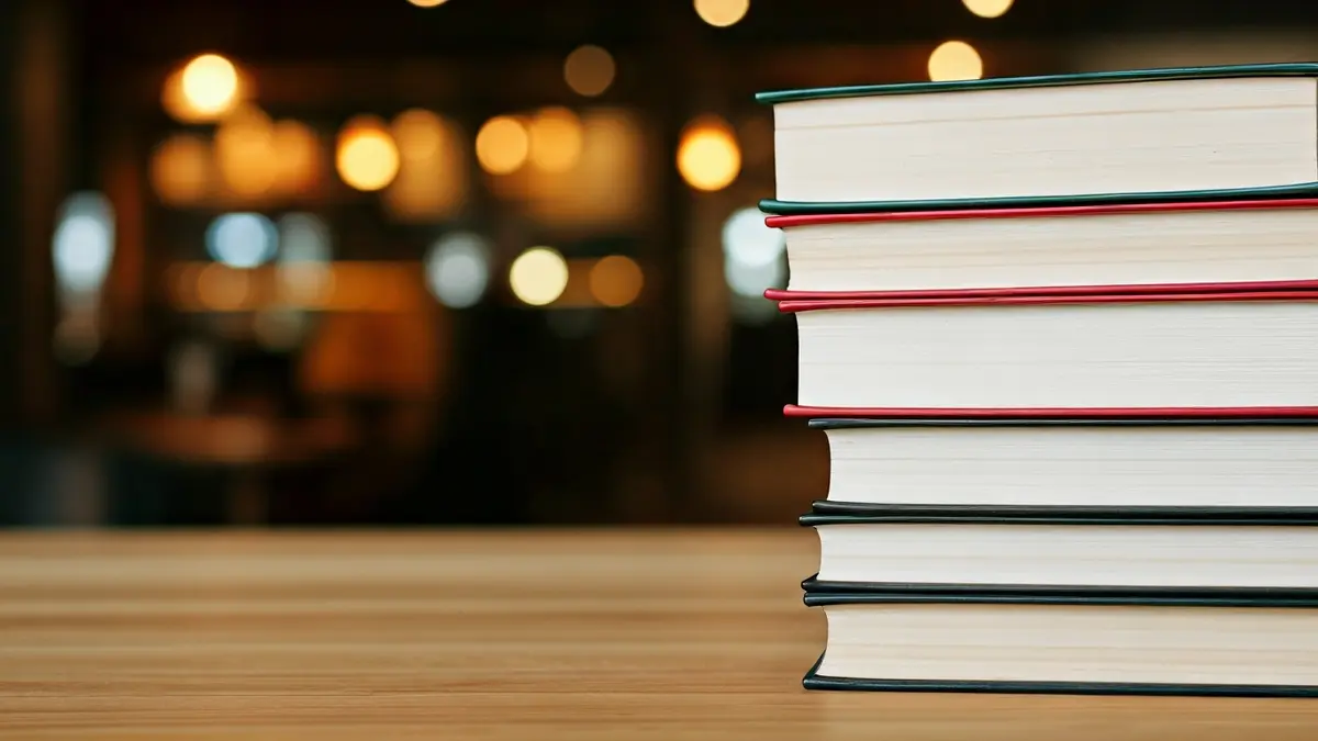 Imagen genérica de libros apilados en una mesa, con un fondo desenfocado de una biblioteca.