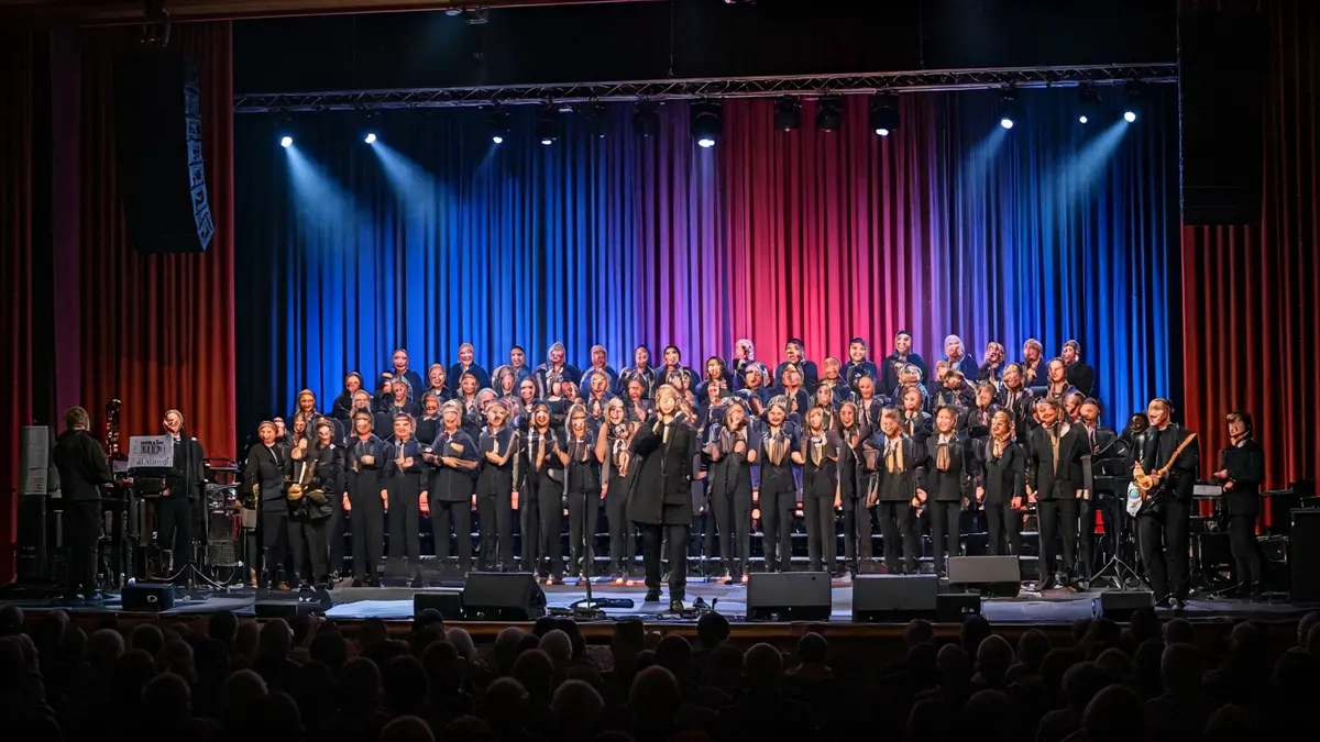 Image of a choir performing on a stage with dynamic lighting and a live band.