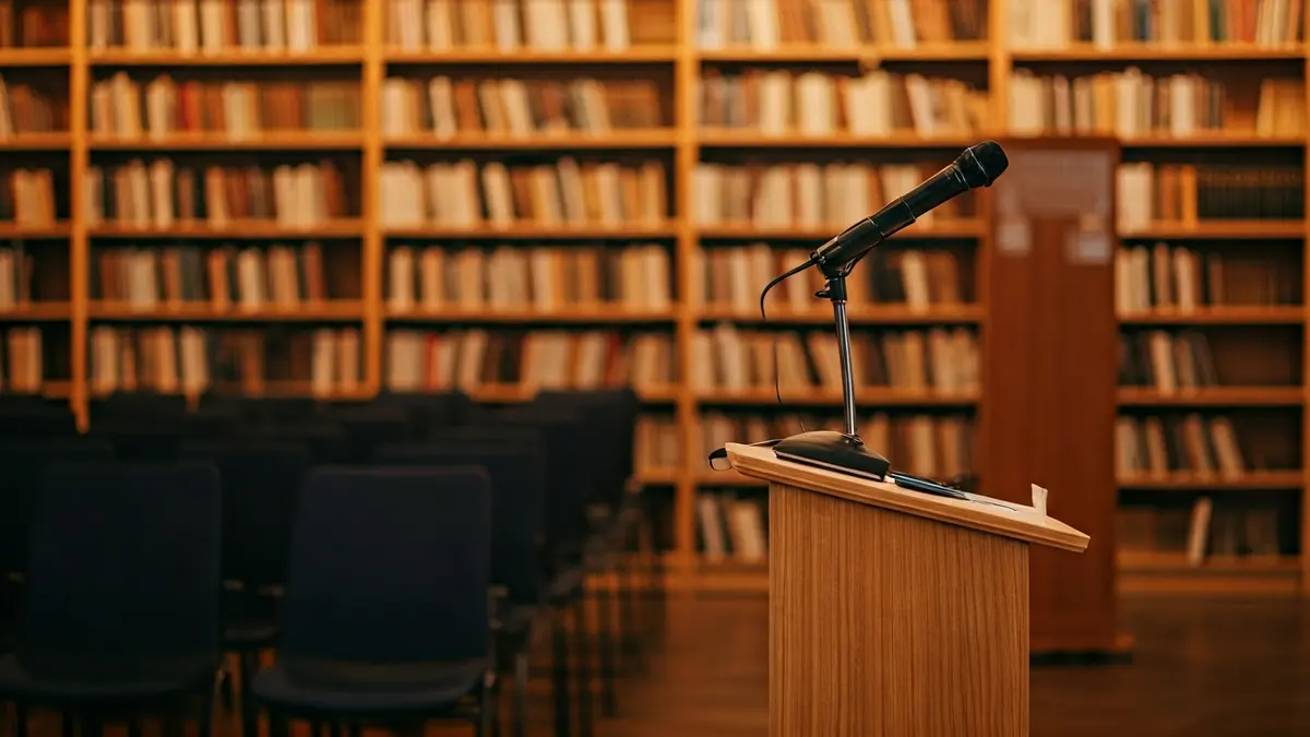 Generic image of a library with wooden bookshelves and a podium with a microphone, with warm lighting.