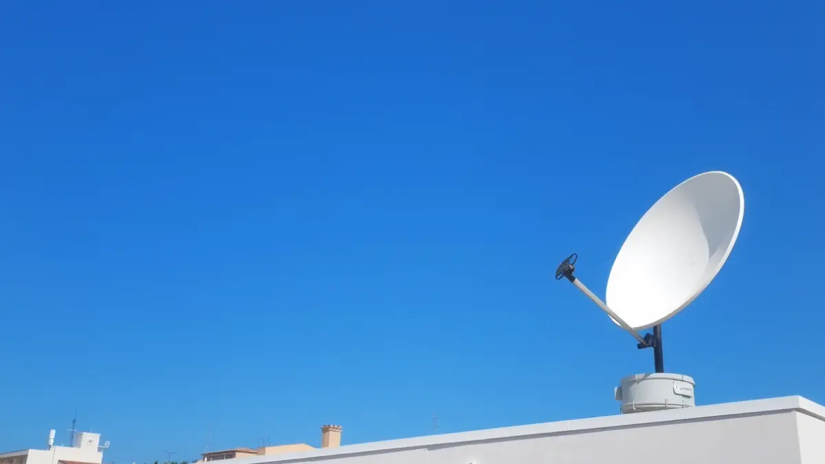 Imatge d'una antena satel·litària en la teulada d'un edifici municipal, amb un cel blau clar, simbolitzant la comunicació i la seguretat.