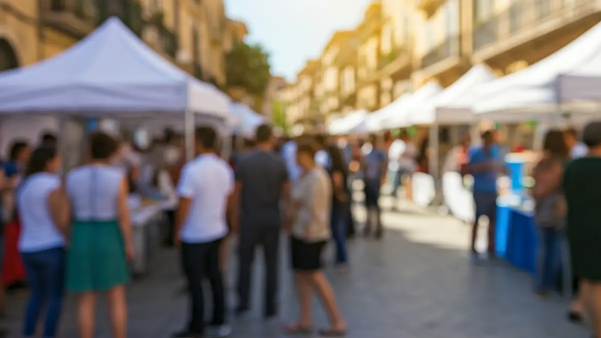 Imagen genérica de una feria educativa en una calle mediterránea, con puestos y una carpa central, gente interactuando, luz diurna cálida.