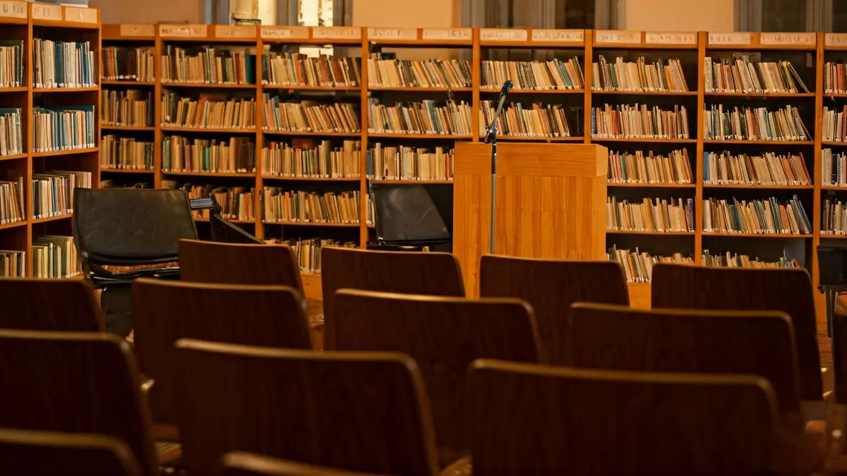 Generic image of a library interior with wooden bookshelves and a podium with a microphone.
