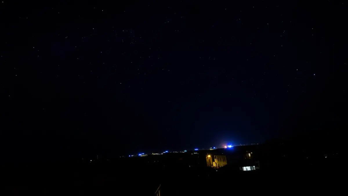 Imagen genérica de un cielo nocturno estrellado sobre una ciudad mediterránea con luces de emergencia azules lejanas.