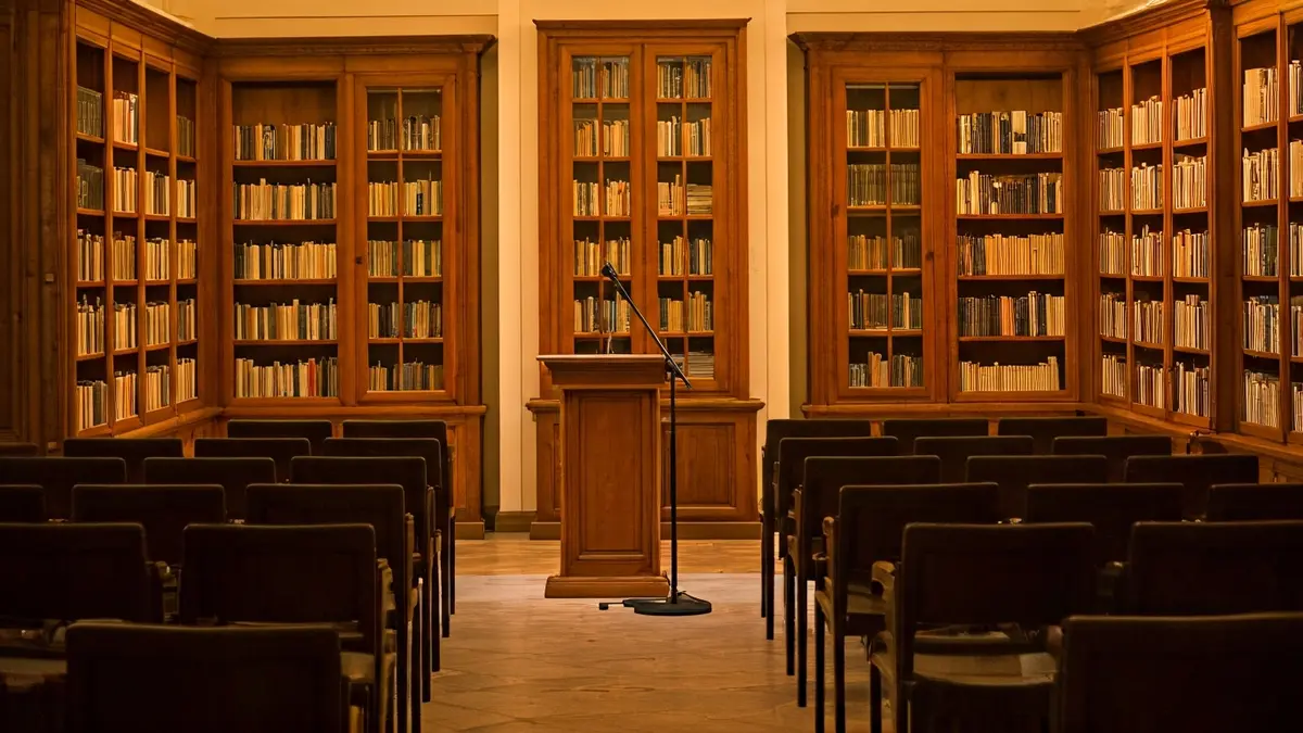 Imatge genèrica d'una sala de conferències o biblioteca amb un podi i cadires buides, il·luminada càlidament.