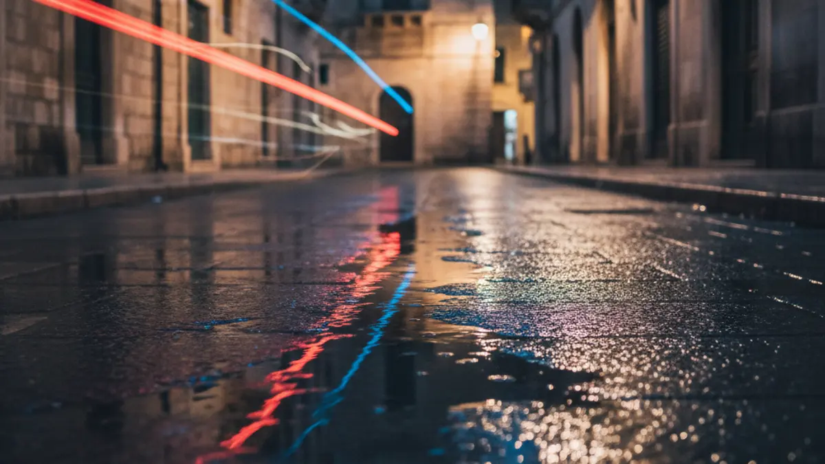 Imatge genèrica de llums d'emergència reflectint-se en l'asfalt mullat de nit, sense vehicles visibles, en un entorn urbà mediterrani.
