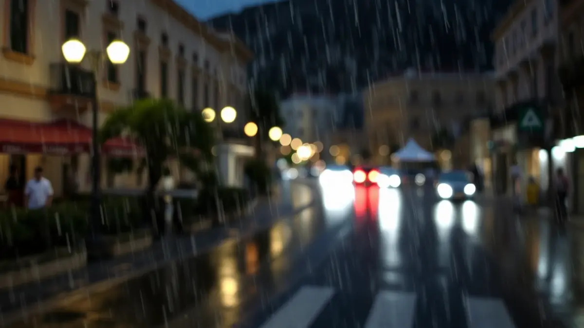 Imatge genèrica de pluja en un carrer d'una ciutat mediterrània, amb edificis i fanals borrosos.