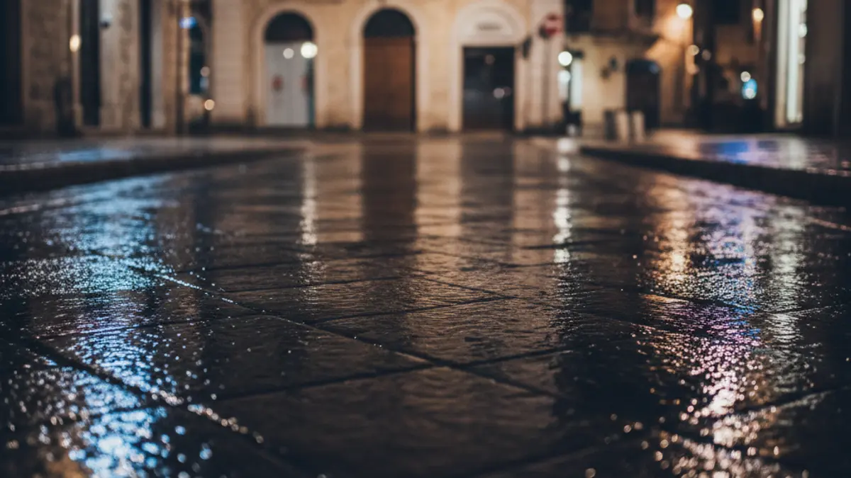 Generic image of emergency lights reflecting on wet asphalt at night, with no visible vehicles, in a Mediterranean urban setting.