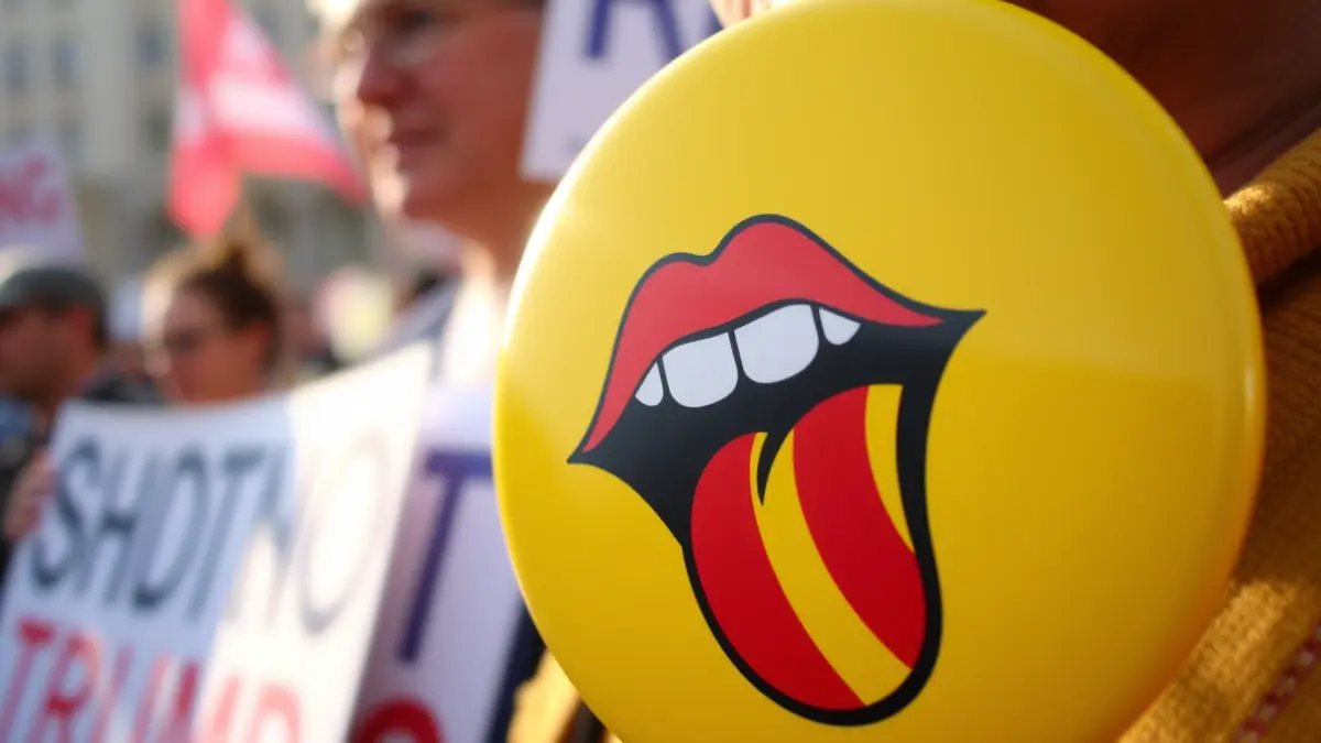 Imatge d'un adhesiu amb una boca i una llengua amb les quatre barres, símbol de suport a la llengua valenciana, en el context d'una manifestació.