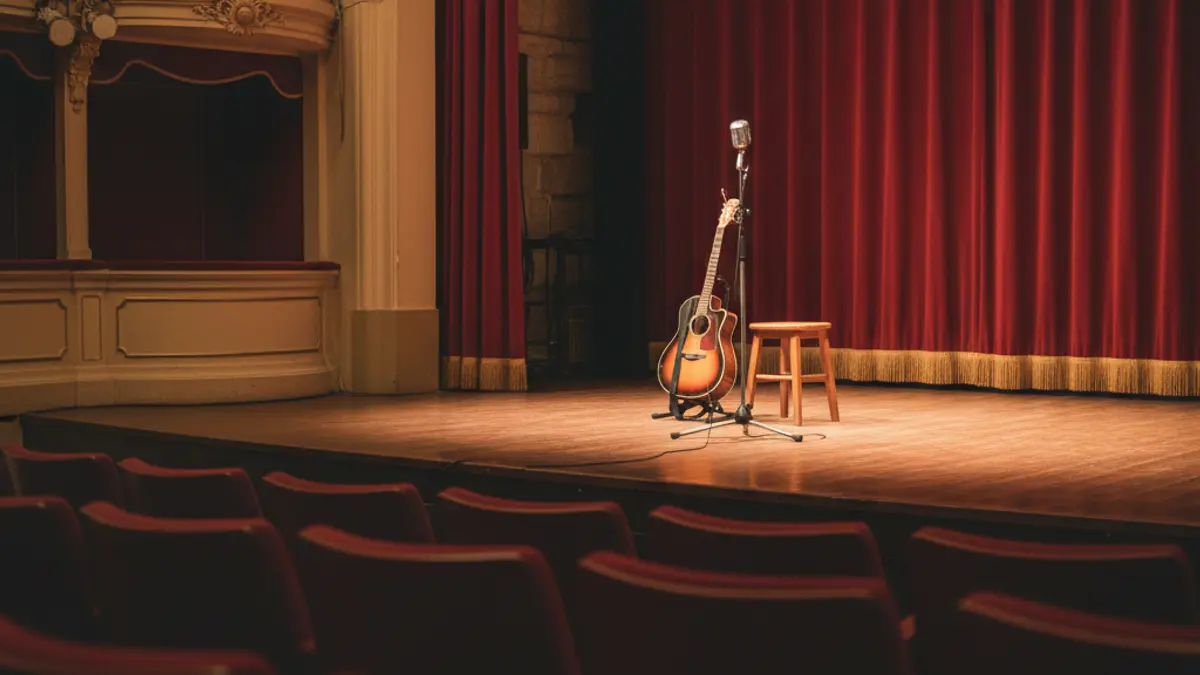Imagen genérica de un escenario de teatro con un micrófono y una guitarra, luces cálidas.