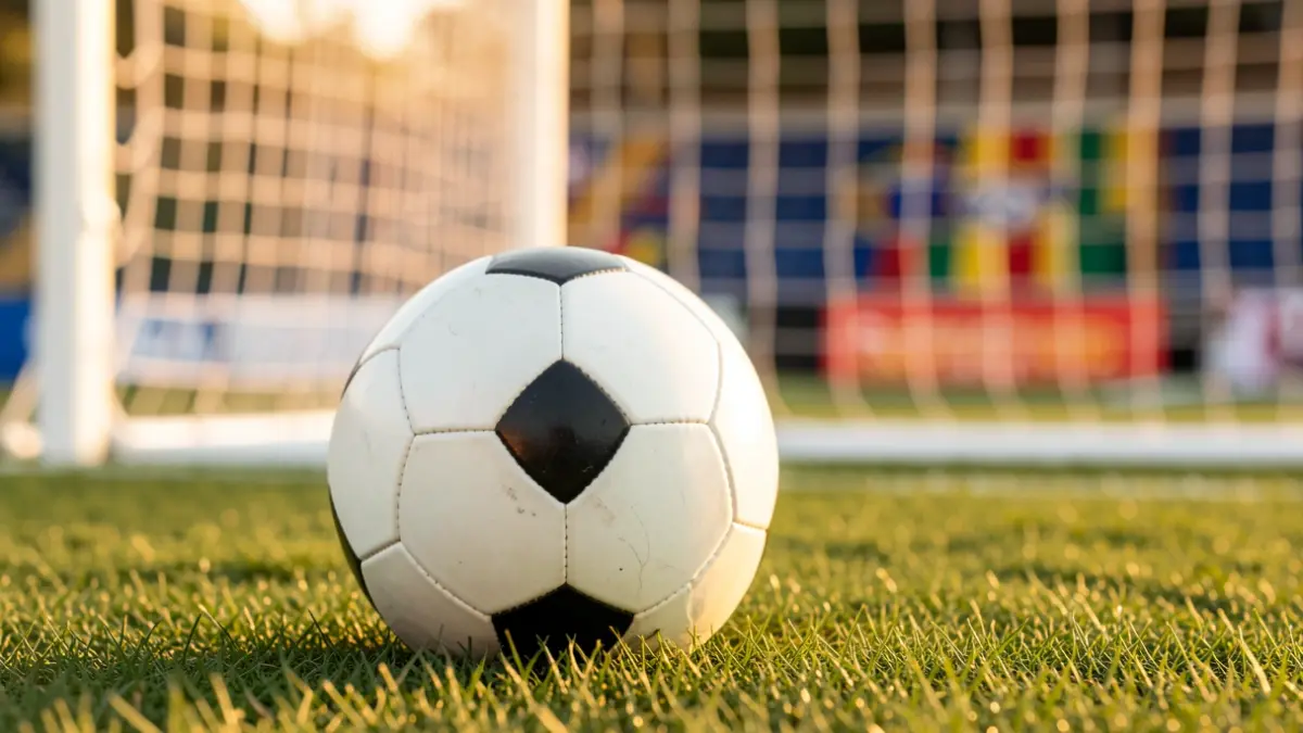 Generic image of a soccer ball on grass with the goal net blurred.