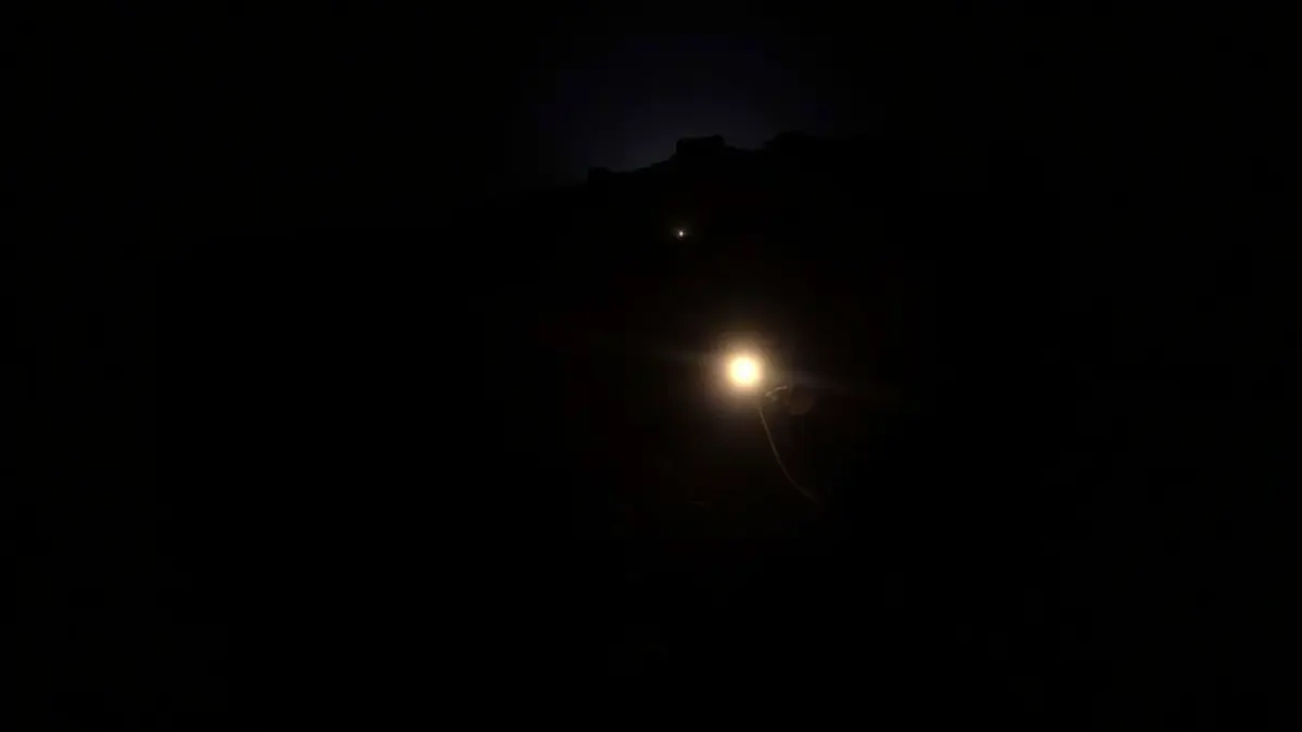 Imagen de luces de emergencia reflejándose en un camino de montaña oscuro durante la noche, con siluetas borrosas de árboles.