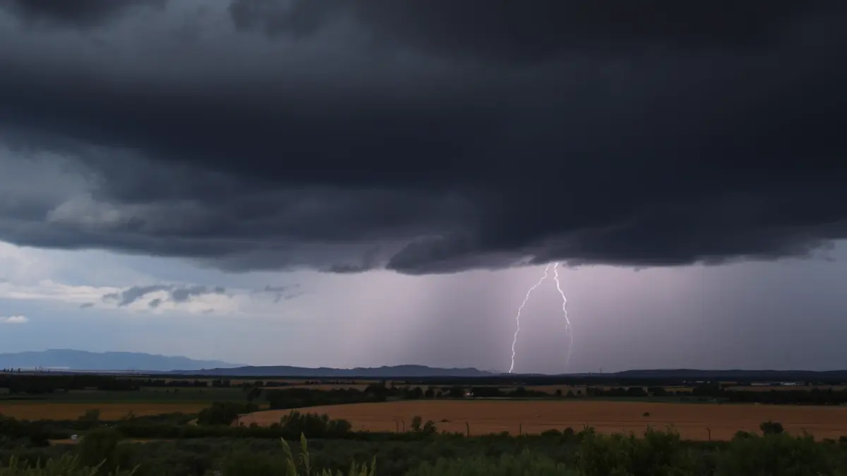 Imatge genèrica de núvols de tempesta sobre un paisatge rural valencià, amb llamps llunyans i pluja intensa.